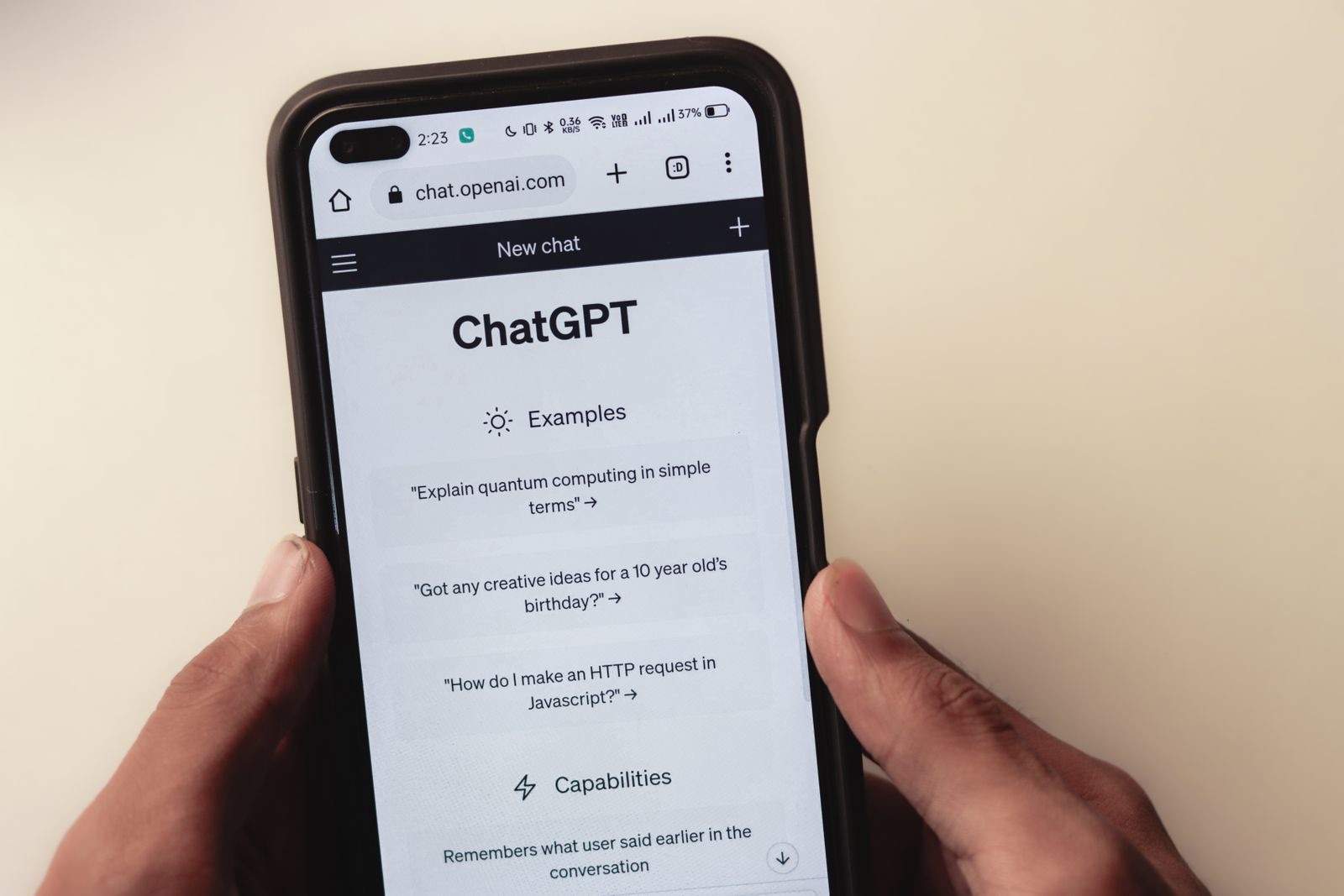 Close-up of a hand holding a smartphone displaying the ChatGPT AI chatbot conversational interface with examples and capabilities