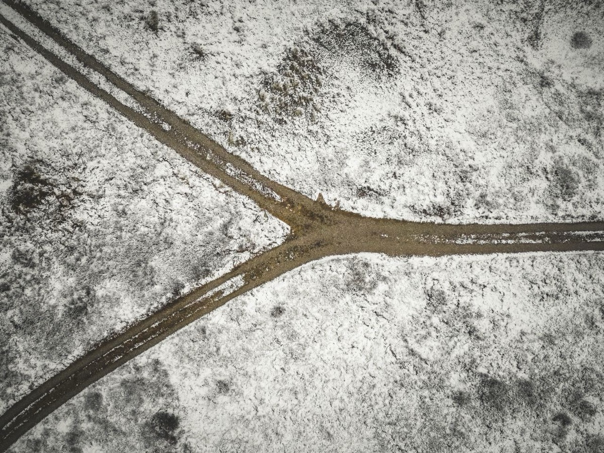 A dirt road forking into two directions across a minimal snowy landscape, a clean metaphor for diverging strategies