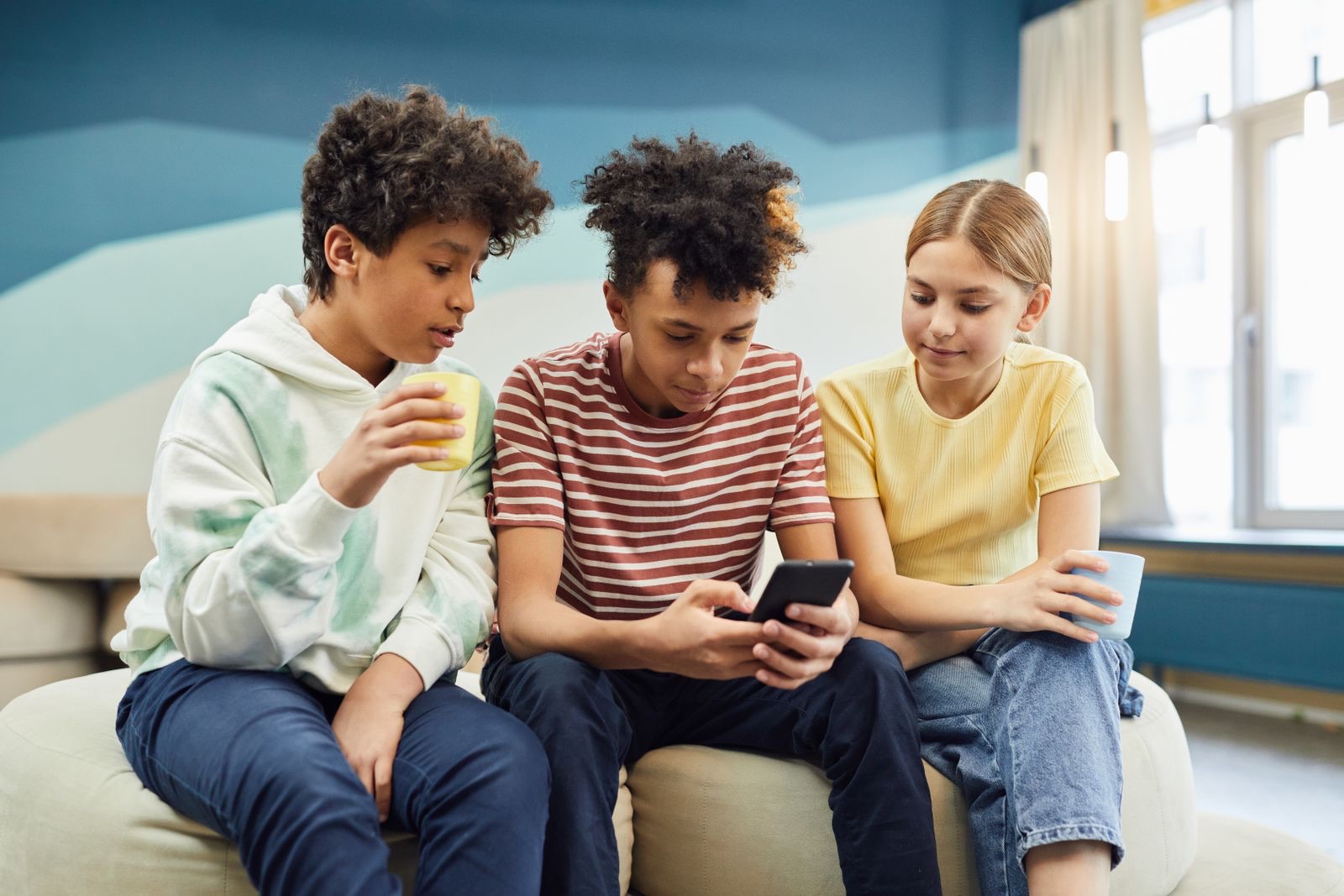 Group of diverse young friends gathered together looking at and discussing content on a shared smartphone, representing an online community and social conversation